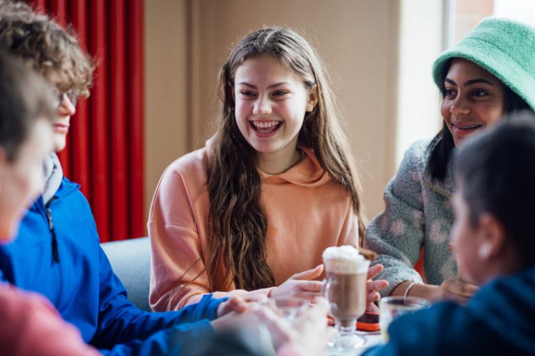 A group of male and female teenagers enjoying a weekend hanging out together in Whitley Bay, North East England. They are sitting in a cafe, enjoying hot chocolate refreshments while talking and laughing with each other.
