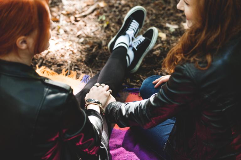High angle of lesbian girls holding their hands sitting on blanket in the park